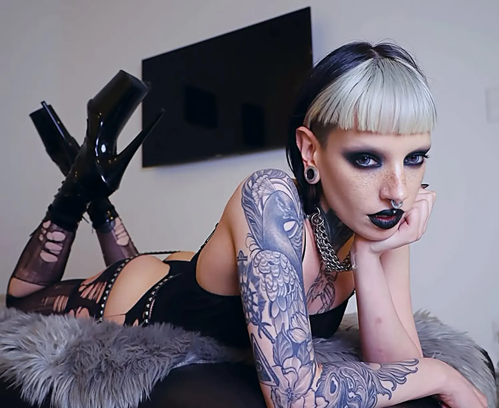Eva Nexus posa com o seu característico visual alternativo, cabelo bicolor, tatuagens completas e maquilhagem escura, usando lingerie preta e botas de salto alto.